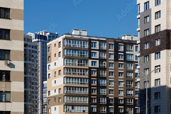 Obraz City view on a sunny day. Modern building and houses against the blue sky.