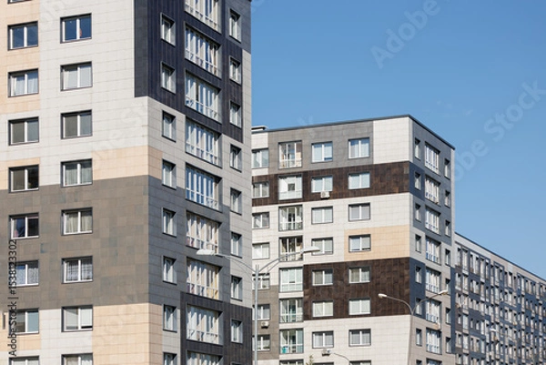 Obraz City view on a sunny day. Modern building and houses against the blue sky.