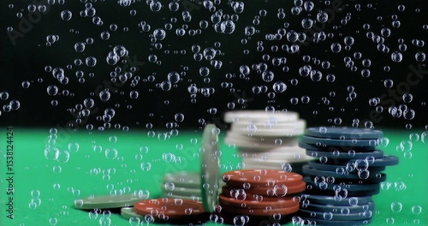 Fototapeta Showing stacks of gaming chips resting on green felt surface, with drifting air bubbles