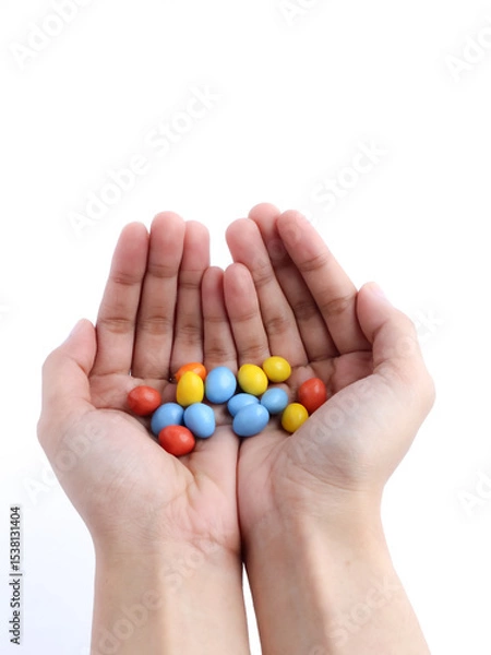 Fototapeta Cupped hands holding colorful candy-coated chocolates on a white background