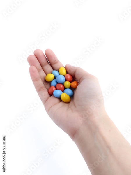 Fototapeta hand holding colorful candy-coated chocolates on a white background