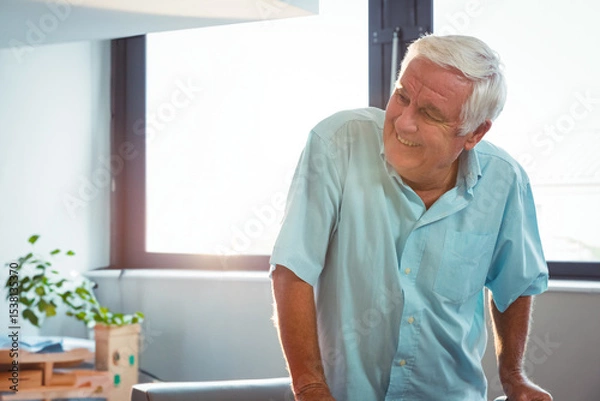 Obraz Senior man leaning on table in bright workspace with potted plant and stacked boxes, copy space