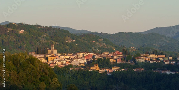 Fototapeta Scenic view of Barga town in Tuscany, Italy, nestled in green hills during sunset light.