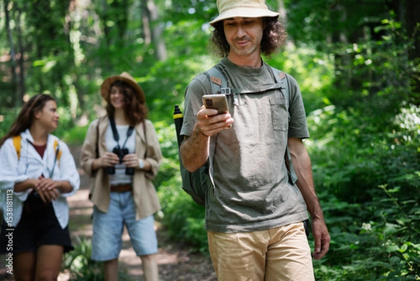 Fototapeta Group of happy young people friends hiking with camera binoculars and backpacks , walking in summer forest