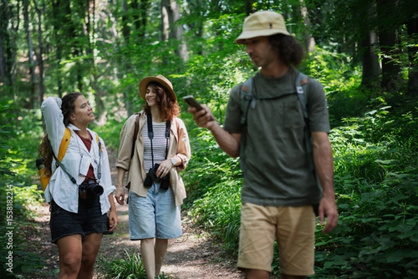 Fototapeta Group of happy young people friends hiking with camera binoculars and backpacks , walking in summer forest