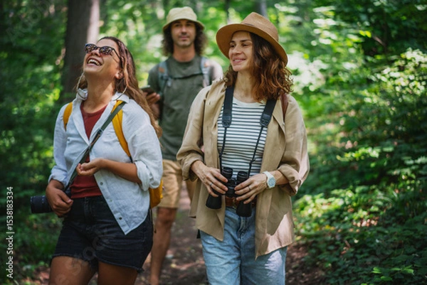 Fototapeta Group of happy young people friends hiking with camera binoculars and backpacks , walking in summer forest