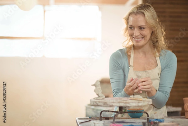Obraz Pottery wheel spinning with wet clay on wooden table in ceramics studio, with small water bowl