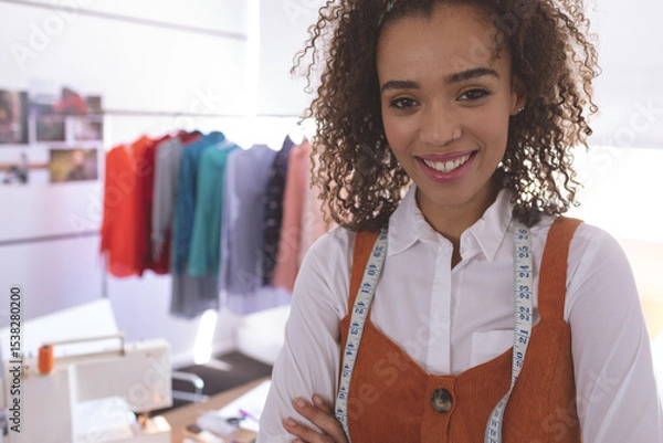 Obraz Fashion designer standing in studio wearing orange jumper with measuring tape, rack in background