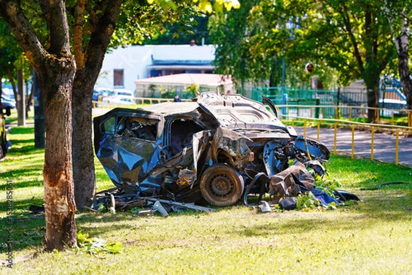 Fototapeta Accident scene with destroyed car on lawn, aftermath of fatal crash with extreme vehicle damage. Crumpled car with front and back obliterated sitting on grassy roadside, devastating collision