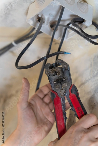 Obraz Electrician is working on electrical wiring, using wire strippers to carefully prepare wires for connection to a junction box during a home renovation or construction project. Vertical photo