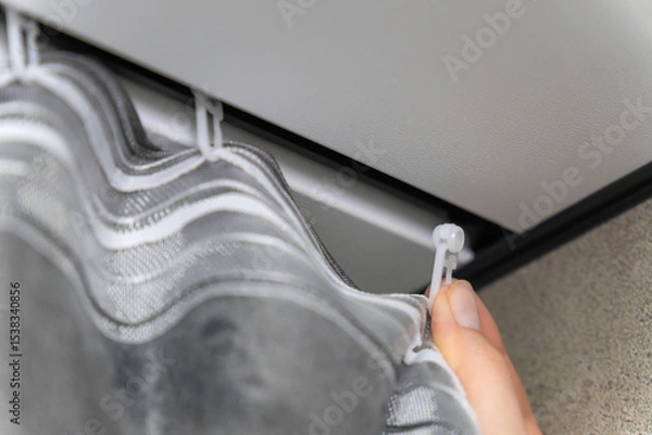 Obraz Worker is attaching a grey curtain to a ceiling-mounted rail using white cable ties, demonstrating a practical and cost-effective method for hanging curtains