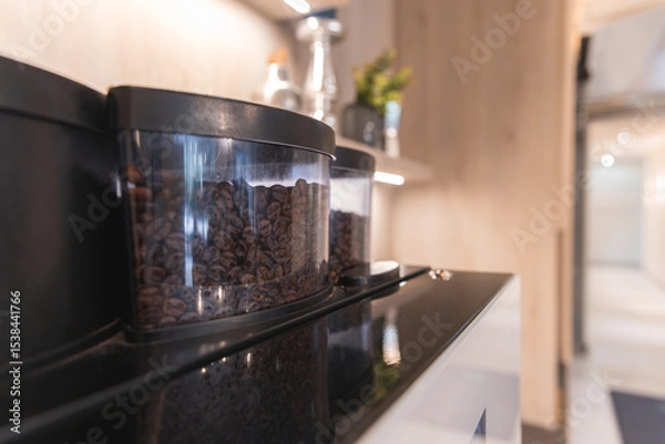 Obraz A coffee machine with transparent bean containers in a refined interior featuring light wooden paneling, minimal decor, and blurred hallway in the background.