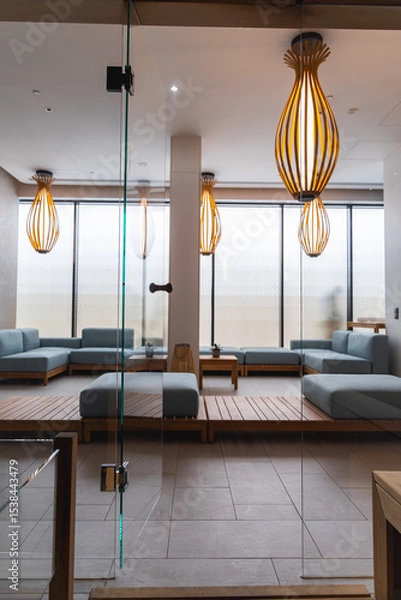 Obraz Luxury hotel spa area with light blue sofas on a wooden platform, wooden pendant lights, frosted windows, and a glass partition for an airy ambiance.