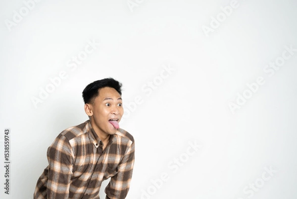 Fototapeta A cheerful young man in casual clothing expressing himself playfully while sticking out his tongue, radiating fun energy.