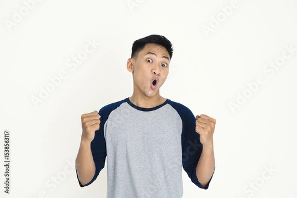 Fototapeta A young man expressing excitement and joy with clenched fists and a vivid facial expression, wearing casual clothing, demonstrating positive emotion, celebration, and personal achievement