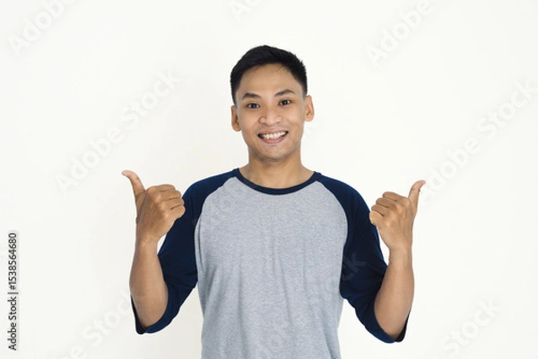 Fototapeta A cheerful individual wearing a casual shirt smiling confidently and gesturing with thumbs up.