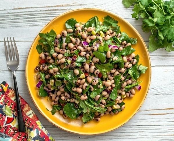 Obraz Overhead shot of a vibrant black-eyed pea salad served on a yellow plate, garnished with fresh herbs and red onion.