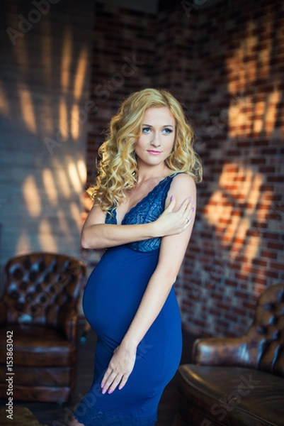 Fototapeta A beautiful red-haired pregnant girl is standing in a nightie.
