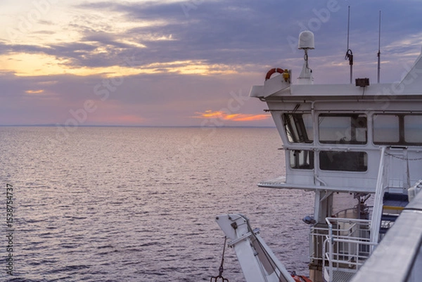Fototapeta A stunning sunset casts vibrant colors across the sea while the ferry cruise ship sails through the tranquil Kattegat Strait, with the bridge in view.
