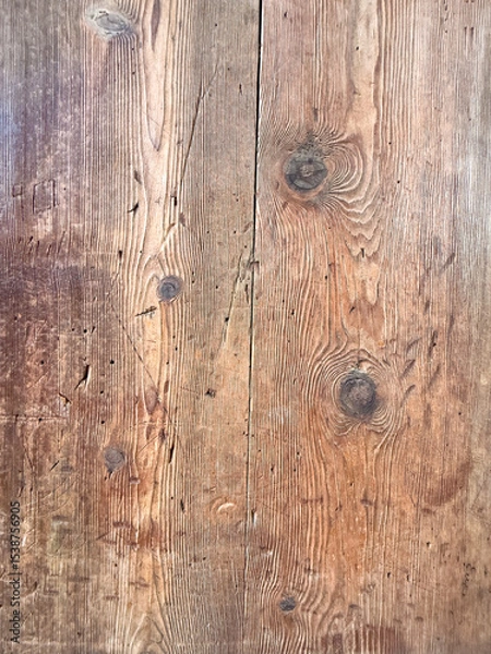 Fototapeta Close-up of a rustic wooden surface with visible grain patterns and knots. The wood has a warm brown tone, showcasing natural textures and imperfections.