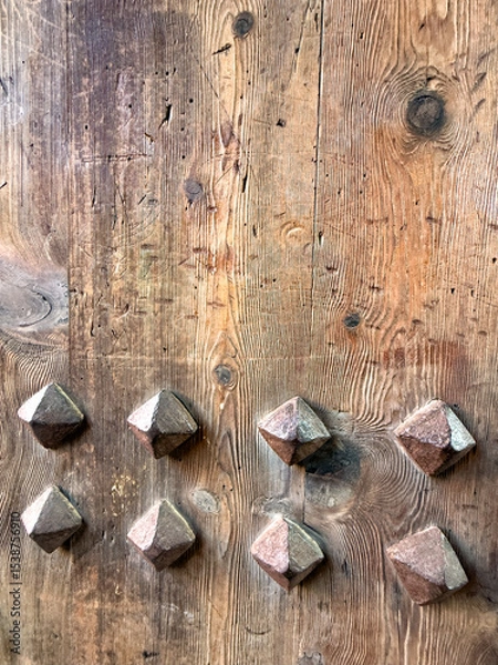 Fototapeta A close-up view of a wooden door with decorative metal studs. The wood has a rustic texture, showcasing natural grain patterns and knots.