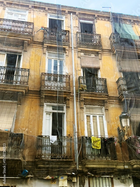 Fototapeta An old yellow apartment building with multiple balconies. Clothes hang on the railings. Windows are partially open, revealing a glimpse of the interior.
