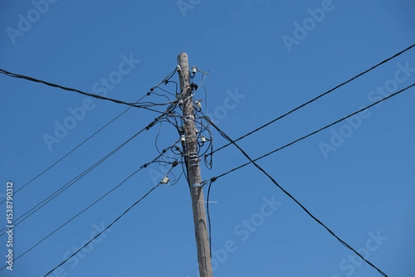 Fototapeta Old wooden pole with wires against blue sky. Electricity and infrastructure concept