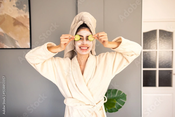 Fototapeta Cheerful Woman In Luxurious Cream Bathrobe With Hair Towel Enjoying Home Spa Treatment With Cucumber Slices