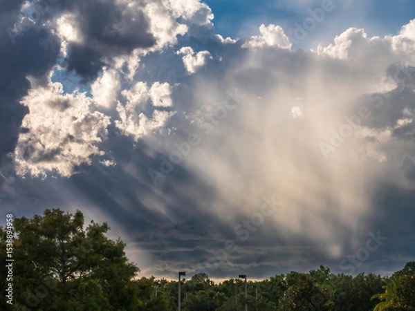 Obraz Saharan dust glows in sunlight slanting through gaps between bright and shadowy clouds on a June evening in southwest Florida, for motifs of seasonal weather and visually dramatic natural phenomena