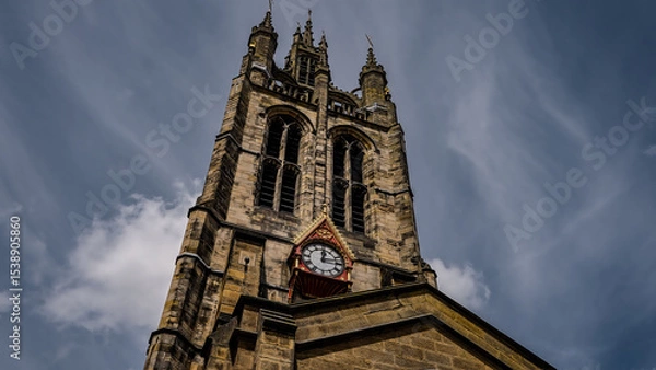 Fototapeta Low angle view of St. Nicholas Cathedral's majestic tower and clock against a backdrop of dynamic clouds