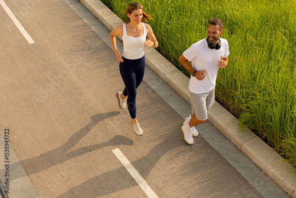 Obraz Joyful morning joggers enjoying the sunshine along a scenic pathway surrounded by green grass and vibrant nature