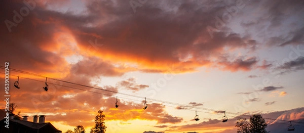 Fototapeta Scenic sunset view with vibrant orange and purple clouds, silhouetted ski lift cables, and distant mountains creating tranquil atmosphere for outdoor enthusiasts and nature lovers