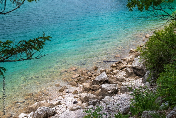 Fototapeta A serene alpine lake with crystal-clear turquoise water mirrors the snow-capped Zugspitze and pine-covered hills. Rowboats glide gently under a clear blue sky—pure alpine tranquility.