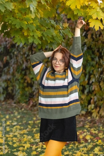 Fototapeta Portrait of a young beautiful red-haired girl in an autumn city park.