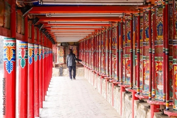 Fototapeta A pilgrim walks beside the longest Tibetan prayer wheels at Labrang Monastery during the Butter Lamp Festival in Amdo, a historic region of Greater Tibet.