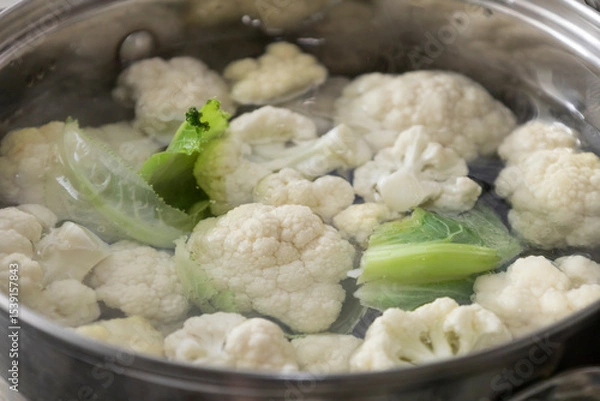 Fototapeta Fresh cauliflower is boiled in a saucepan with water. The vegetable is divided into florets and boiled in a saucepan.