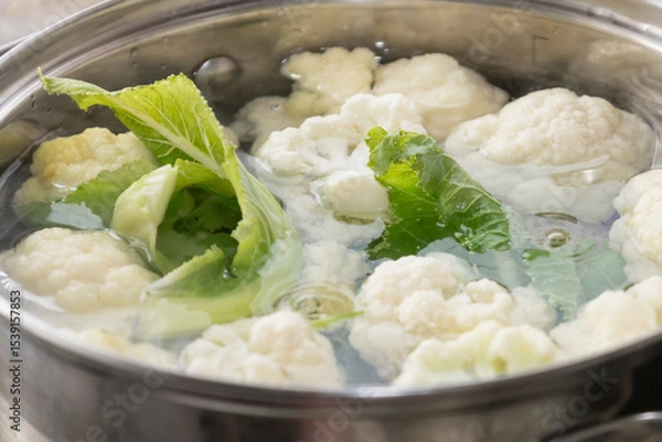 Fototapeta Fresh cauliflower is boiled in a saucepan with water. The vegetable is divided into florets and boiled in a saucepan.