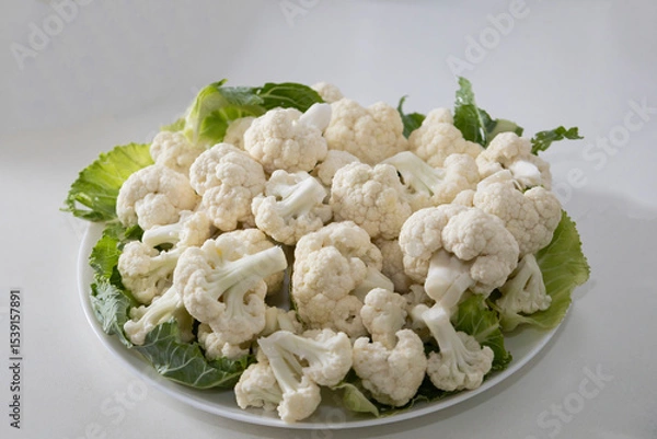 Fototapeta Fresh and raw cauliflower on the white plate.  The cauliflower  -  vegetable is cut into pieces on white background. The vegetable is divided into inflorescences on the plate