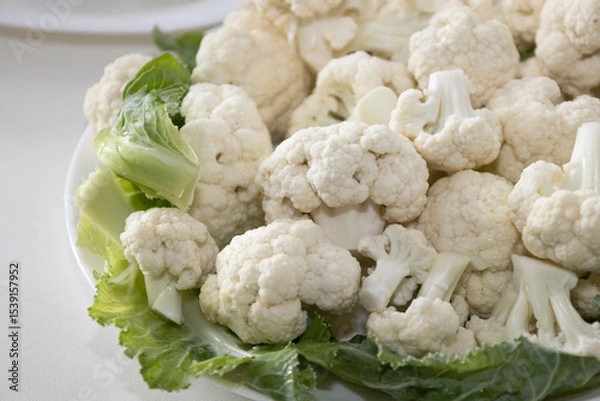 Fototapeta Fresh and raw cauliflower on the white plate.  The cauliflower  -  vegetable is cut into pieces on white background. The vegetable is divided into inflorescences on the plate