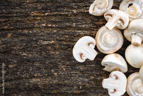 Fototapeta Top view of fresh white mushrooms sliced and whole on rustic dark wooden background with copy space. Organic vegetarian food and cooking ingredient concept