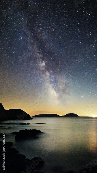Obraz A breathtaking view of the night sky showcasing the Milky Way, perfectly illuminated over the tranquil ocean, casting an enchanting glow on the landscape.