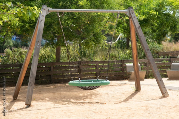 Obraz Modern playground featuring a nest swing with a round woven seat, suspended by ropes from a wooden and metal A-frame. The swing stands on a sandy surface. Ideal outdoor recreational space for children
