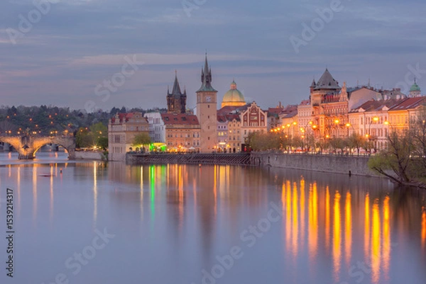 Fototapeta Colorful buildings and towers along the Vltava River in Prague Czech Republic at sunset with calm water and vibrant sky
