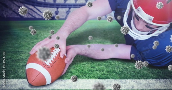Obraz Diving football player in red helmet, jersey placing ball on stadium goal line, virus particles