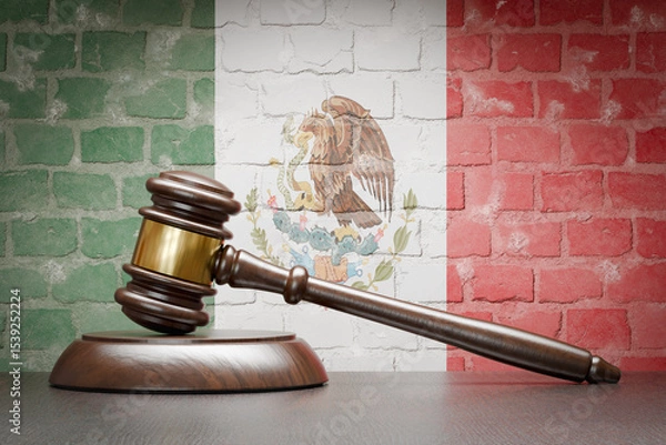 Fototapeta Wooden Gavel Resting on Table In Front of A Brick Wall with Mexican Flag.
