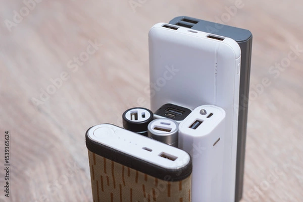 Obraz Assortment of portable power banks in various designs on a wooden surface. Portable chargers for gadgets.