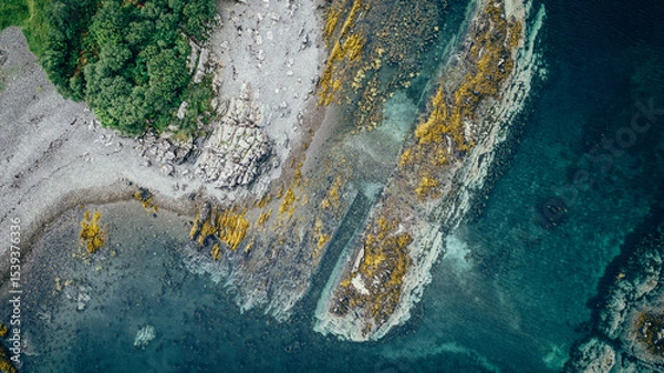 Obraz Aerial view of rocky coastline with green trees and clear blue water on a sunny day landscape shot