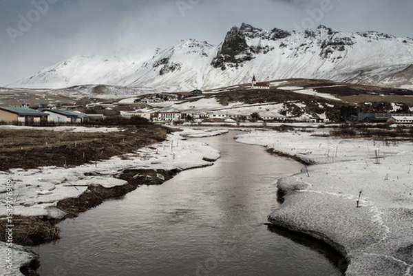 Obraz A winter landscape featuring a river flowing through a valley with snow covered mountains behind it