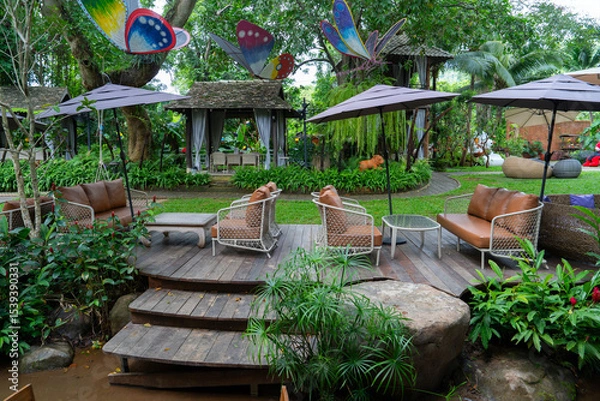 Obraz Outdoor seating area with wooden deck, surrounded by lush greenery and colorful butterfly decorations. Relaxing atmosphere