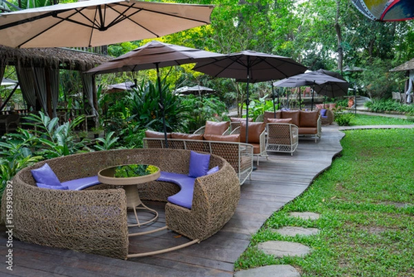 Obraz Outdoor seating area with wicker furniture and umbrellas in lush garden setting. Relaxing atmosphere